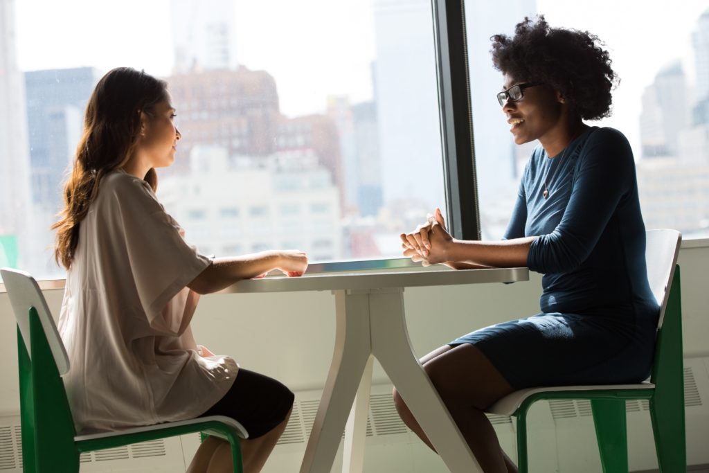 Two people talk at a table by a window