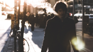 Young man, bundled up, walking down a city street with his breath visible in the cold air.