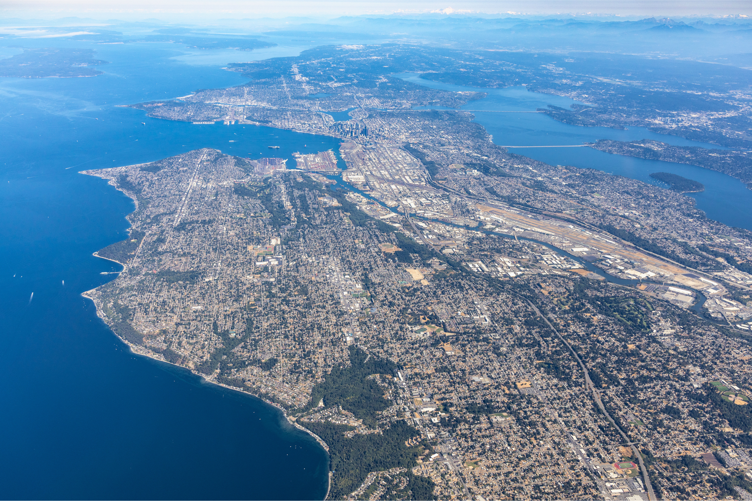 Aerial shot overlooking north over Seattle, including Elliott Bay, the Salish Sea/Puget Sound, Lake Washington, Mercer Island, and parts of the East Side of King County and the Cascade Mountain Range