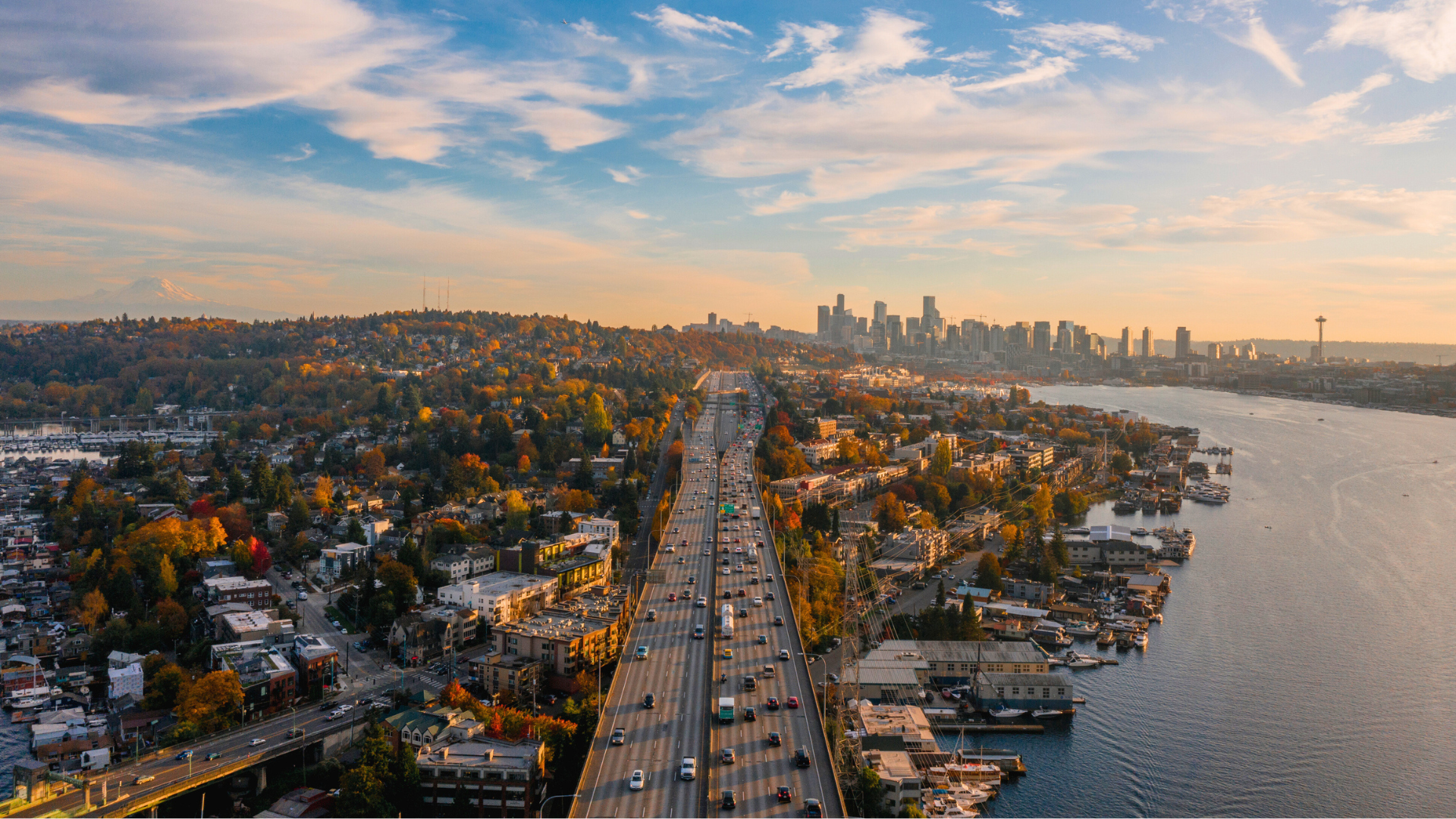 An aerial shot taken from above I-5, looking south over Lake Union on the right, and the East Lake neighborhood on the left, toward the Downtown Seattle skyline, with Mt. Rainier in the far distance.