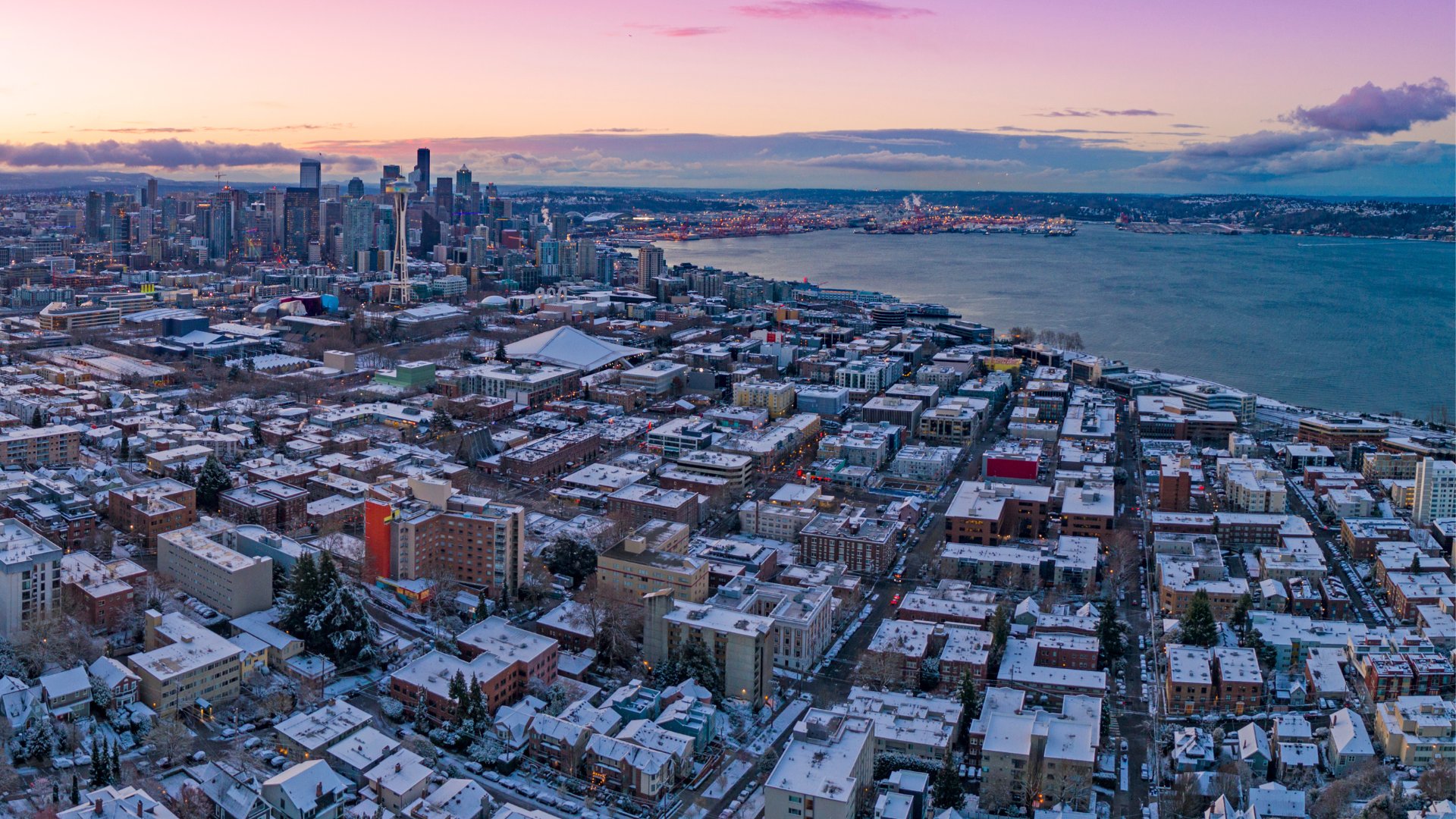 A panoramic view of downtown Seattle, Belltown, Uptown, and Elliott Bay, with snow-covered rooftops and a cold-looking sunset.