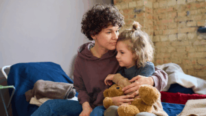 Image is of a parent and child sitting on a cot.